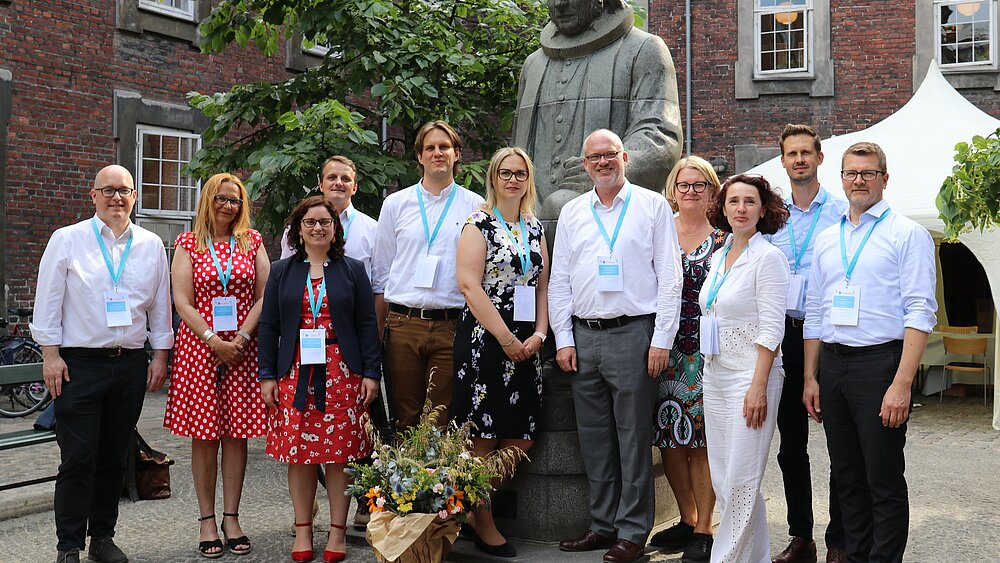 Eine Gruppe Menschen steht in einem Innenhof und lächelt in die Kamera.