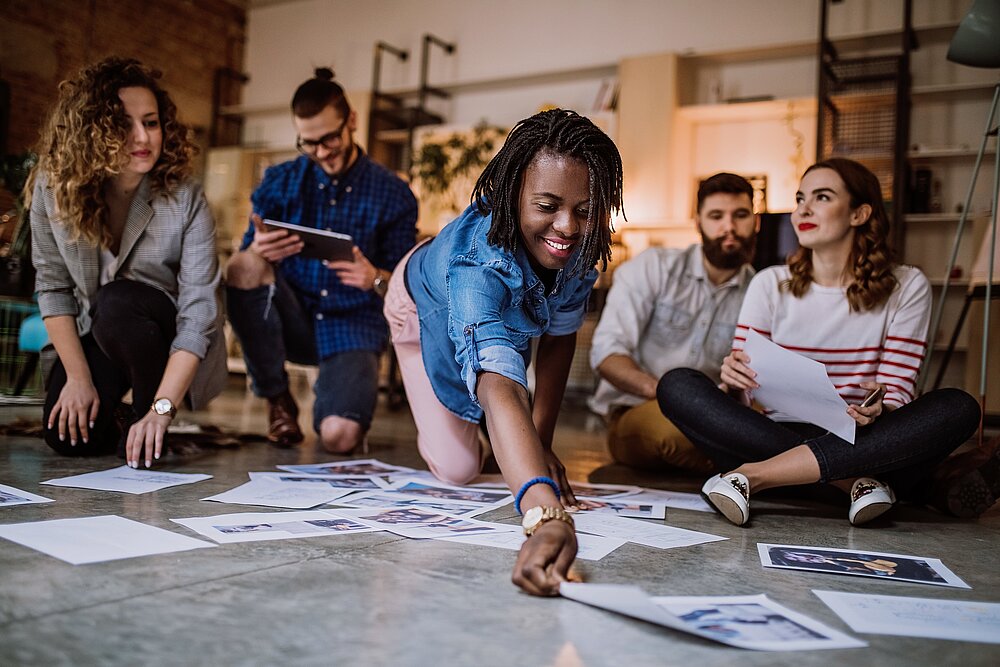 Gruppenarbeit. Junge Frau breitet auf dem Boden Arbeitsblätter aus.