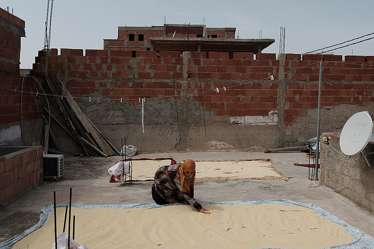 Nabila trocknet Couscouskörner auf dem Dach ihres Hauses in Nâassen. Nabila ist nie zur Schule gegangen. Im Landwirtschaftszentrum von Chbedda lernte sie Lesen und Schreiben und entschied sich dann für den Beruf der Kunsthandwerkerin. Sie verkauft ihre Waren auf den Märkten oder an die örtlichen Händler*innen. Diese Tätigkeit hat es ihr ermöglicht, finanziell unabhängig zu werden und ihre Familie zu unterstützen. DVV International. ©Augustin Le Gall