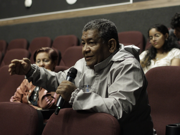 Ein Mann sitzt in einem Kinosaal und spricht in ein Mikrofon.