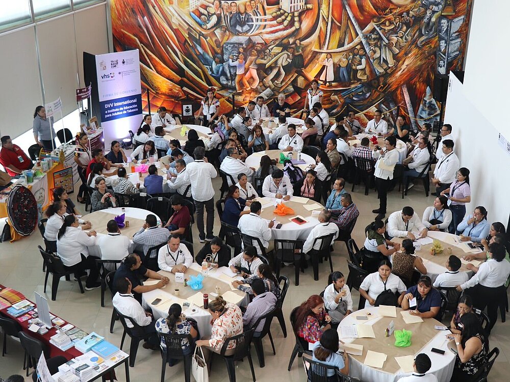 Blick von oben auf mehrere Personen, die an runden Tischen zusammen sitzen.